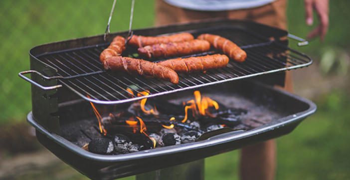 Mann grillt Würstchen auf Holzkohlegrill