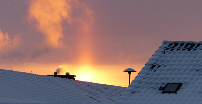 Schornstein mit Rauch auf schneebedecktem Dach